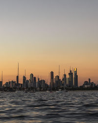 Sea by modern buildings against clear sky during sunset