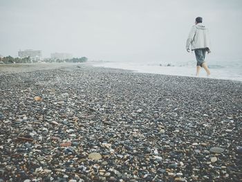 Rear view of man walking at beach against clear sky