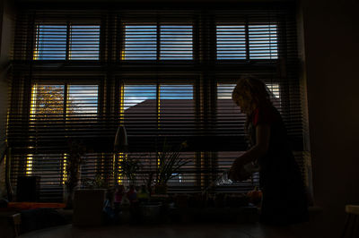 Woman pouring drinking water at dining table by window