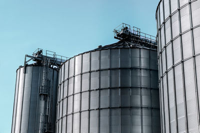 Low angle view of silos against clear blue sky