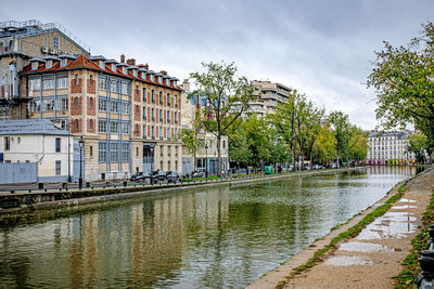 Buildings by river against sky