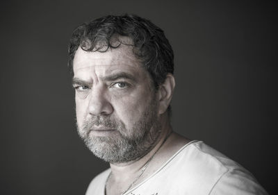 Close-up portrait of serious mature man against gray background