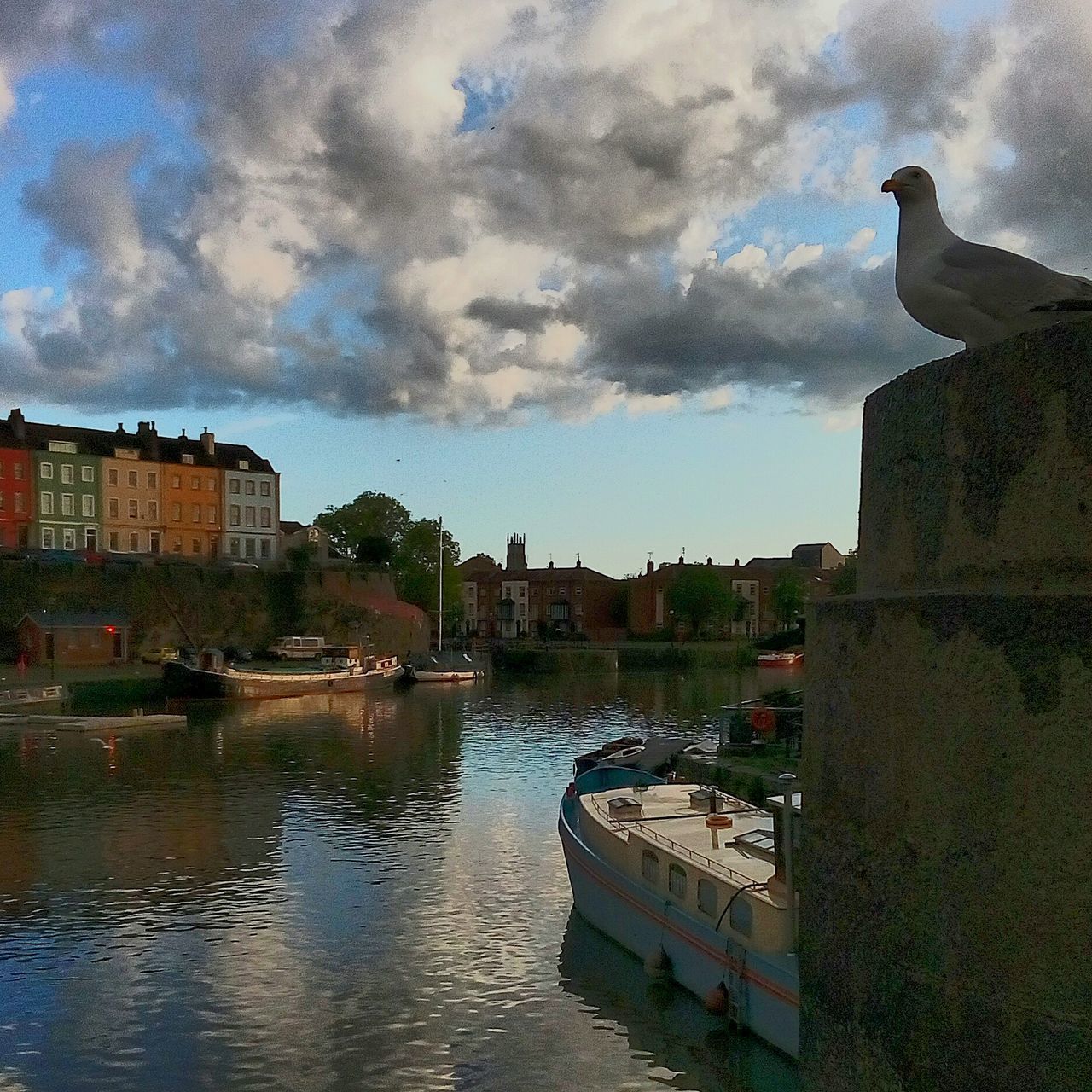 BOATS MOORED IN RIVER BY BUILDINGS AGAINST SKY