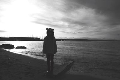 Side view of girl standing on shore at beach against sky during sunset