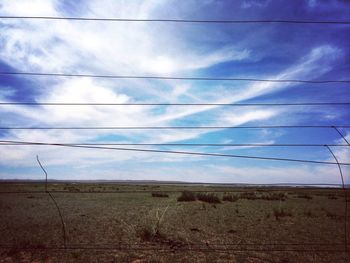 Electricity pylon on field against cloudy sky