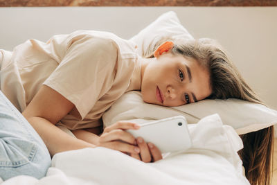 Tired melancholic woman uses mobile phone while lying in bed in apartment.