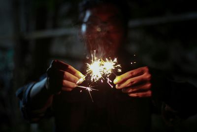 Midsection of woman holding sparkler at night