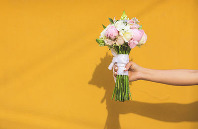 Midsection of person holding bouquet against wall
