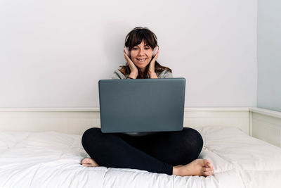 Young woman using mobile phone while sitting on bed