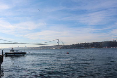 Boats in sea by bosphorus bridge against cloudy sky