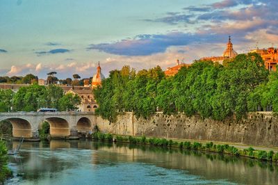 Bridge over river in city against cloudy sky