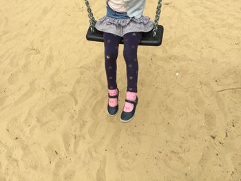 Low section of girl on swing at sandy beach