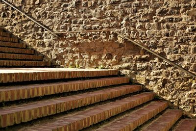 A stairway made of bricks along a stony wall in the sunlight. 