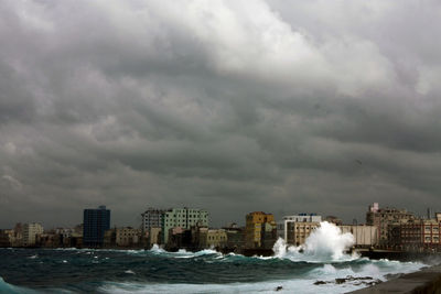 View of city at waterfront against storm clouds