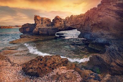 Rocks in sea against sky during sunset