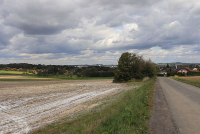 Empty road amidst field against sky