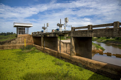 Built structure on field by river against sky