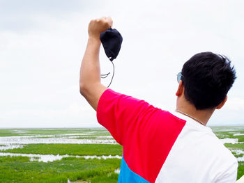 Rear view of man holding camera at beach against sky