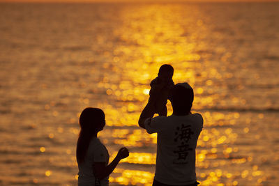 Silhouette couple with baby standing against sea during sunset
