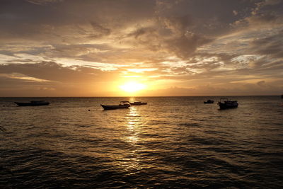 Sunset view with silhouette of traditional fishing boats in the ocean.