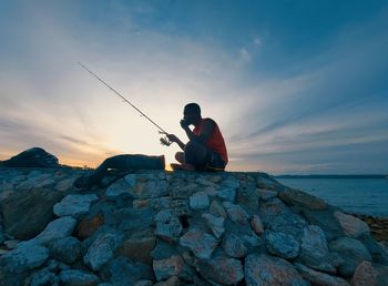 Rear view of man standing on rock at beach against sky