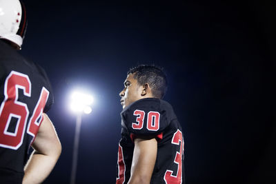 Low angle view of teenage american football player standing against clear sky at night