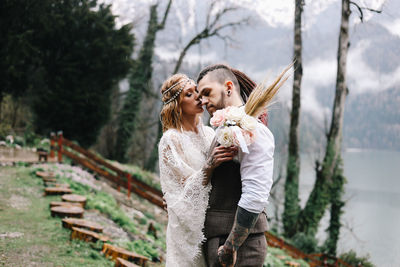 Happy newlyweds in love a man and a woman in wedding clothes embrace on the shore of the lake