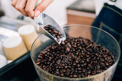 Close up asian woman hand scoops organic coffee beans into an electric coffee grinder.