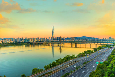 Bridge over river by buildings against sky during sunset