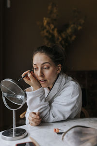 Non-binary person applying make-up while looking in mirror at home