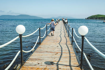 People on pier over sea against sky