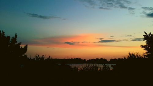 Silhouette trees by lake against romantic sky at sunset