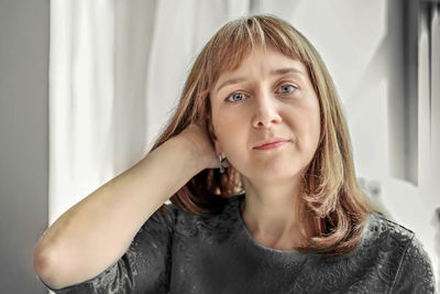 Portrait of a young woman by the window in neutral colors.