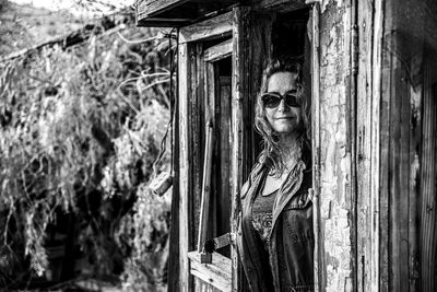 Portrait of smiling woman wearing sunglasses standing at abandoned hut