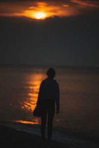 Silhouette woman standing on beach against sky during sunset