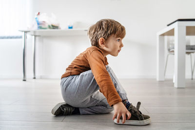 Full length of cute boy sitting on wooden floor at home