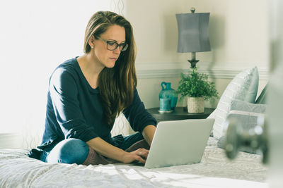 Young woman using phone while sitting on bed at home