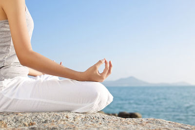 Midsection of woman sitting by sea against clear sky