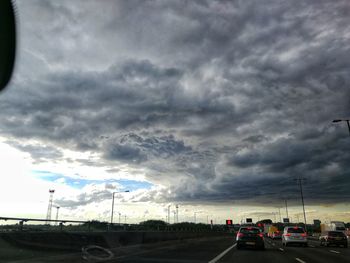 Cars on road against cloudy sky