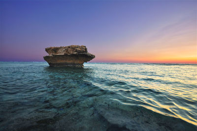 Rock formation in sea against sky during sunset