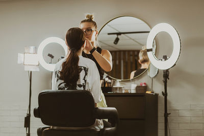 A young makeup artist does makeup to a girl in a salon.