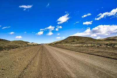 Dirt road along countryside landscape against blue sky