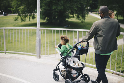 Father walking with children while pushing baby stroller on bridge