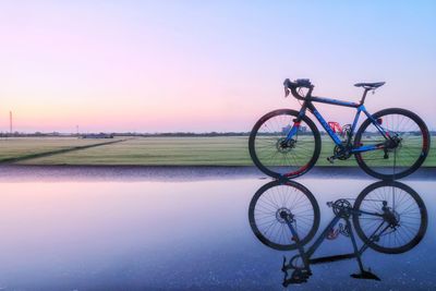 Bicycle by water against clear sky during sunset