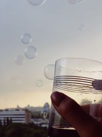 Close-up of hand holding bubbles against sky