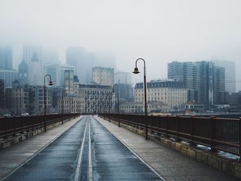 Empty road against buildings during foggy weather