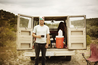 Man holding cup and standing against car on field