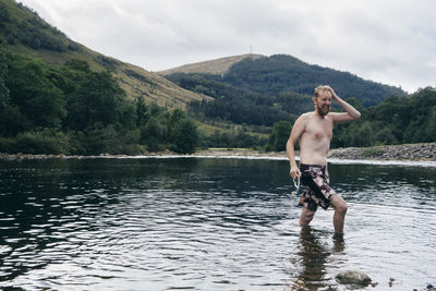 Shirtless man wading in lake against sky