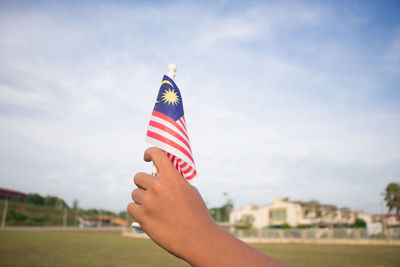 Cropped image of person holding malaysian flag against sky