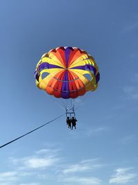 Low angle view of people parasailing against sky